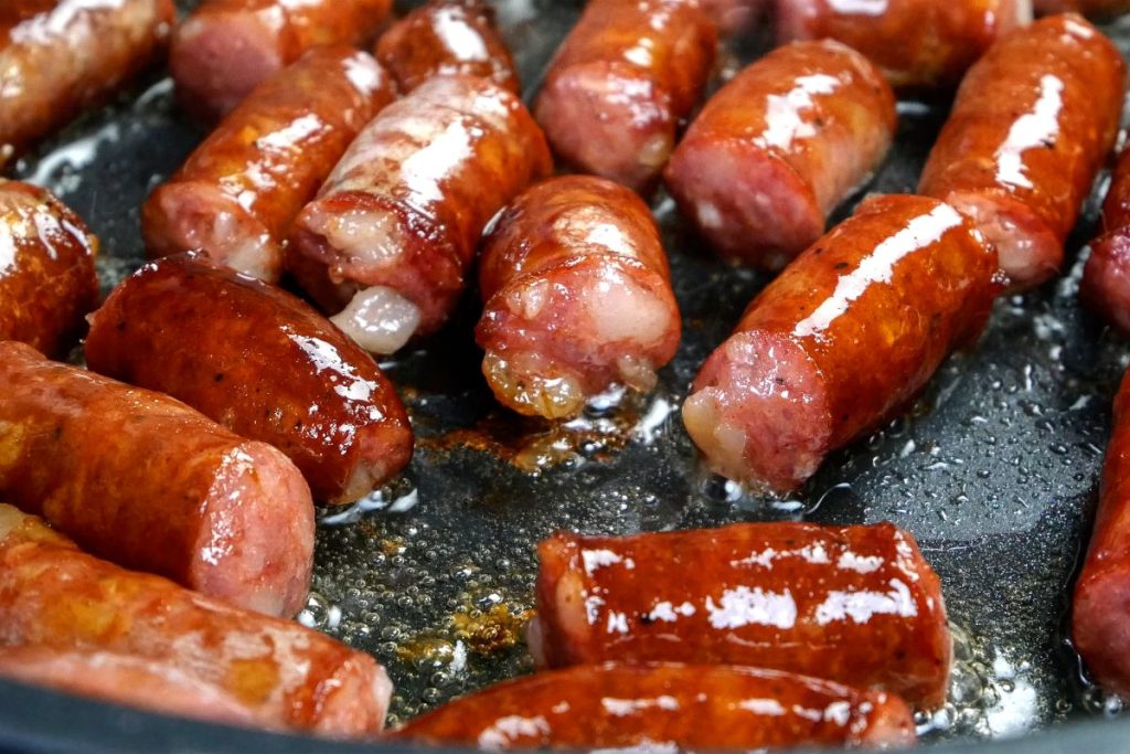 Delicious fatty hunting sausages, cut into pieces, are fried in frying pan in vegetable oil. Fast nutritious food. Home kitchen. Close-up. Indoors.