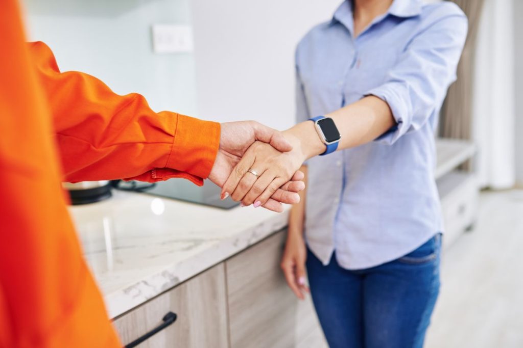 Repairman shaking hand of housewife after finishing work in kitchen