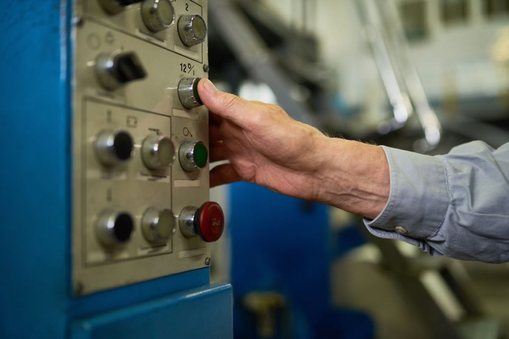 Closeup of unrecognizable senior worker operating machines in factory, hands pressing buttons on control panel