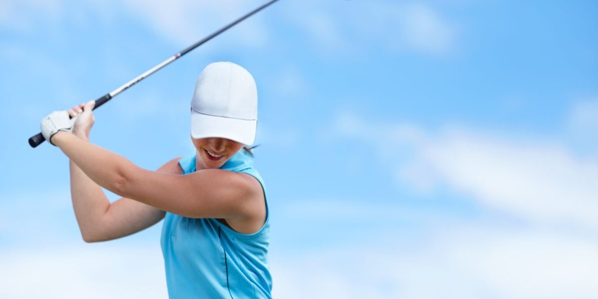 A young female golfer swinging a golf club (driver) over her head about to take a shot - copyspace