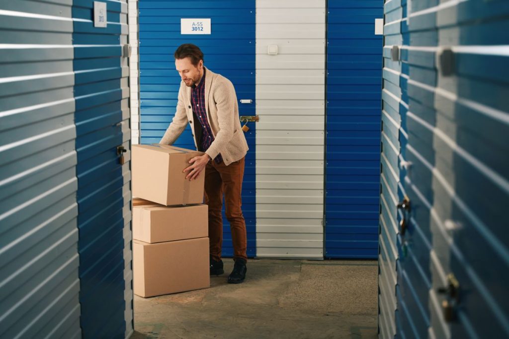 Young man is stacking big cardboard boxes in storage warehouse