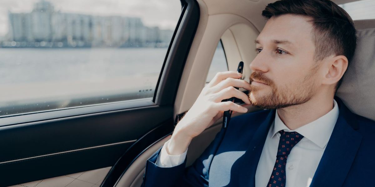 Serious male company executive in blue suit thinking of making important serious decision, weighting in risks and profits, holding his phone against his chin while sitting in limousine
