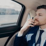 Serious male company executive in blue suit thinking of making important serious decision, weighting in risks and profits, holding his phone against his chin while sitting in limousine