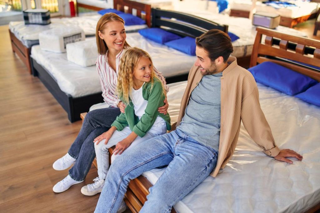 A family with a cute little daughter is choosing a bed in the store. Purchase of a mattress, bed and other sleeping accessories.