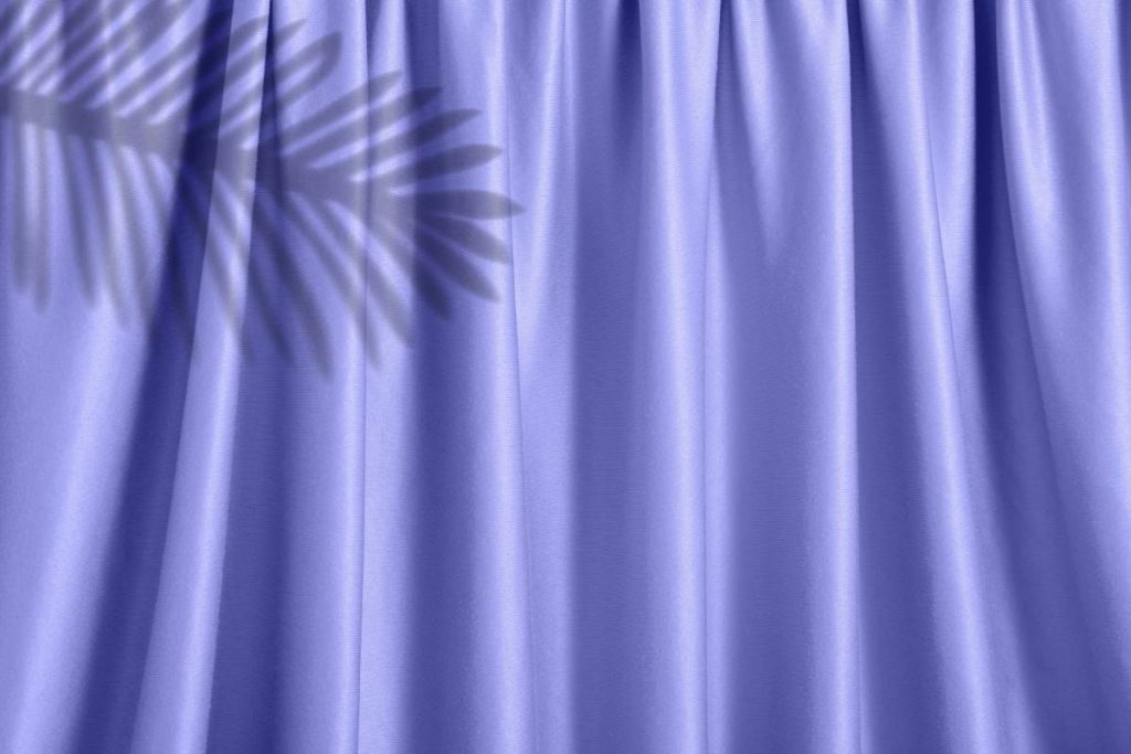A purple curtain illuminated by a bright light source, creating a silhouette of a leaf on the fabric