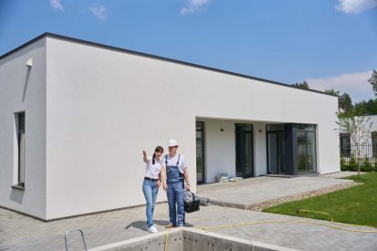 Woman showing something to repairman while they standing by empty swimming pool before repair near new modern townhouse in warm summer day