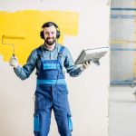 Portrait of a happy repairman listening to the music with headphones during the painting process indoors