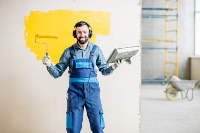 Portrait of a happy repairman listening to the music with headphones during the painting process indoors