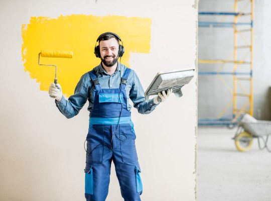 Portrait of a happy repairman listening to the music with headphones during the painting process indoors