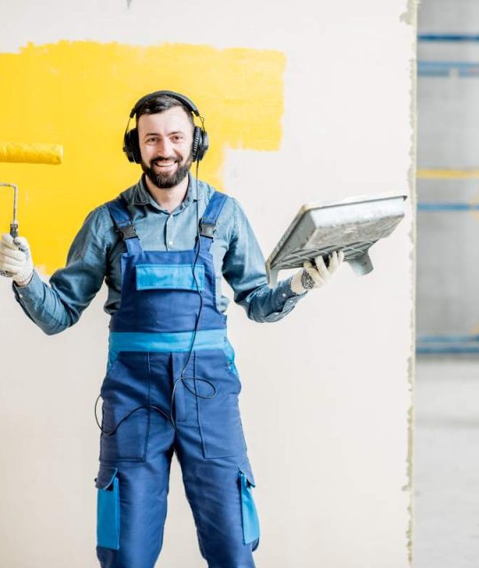 Portrait of a happy repairman listening to the music with headphones during the painting process indoors