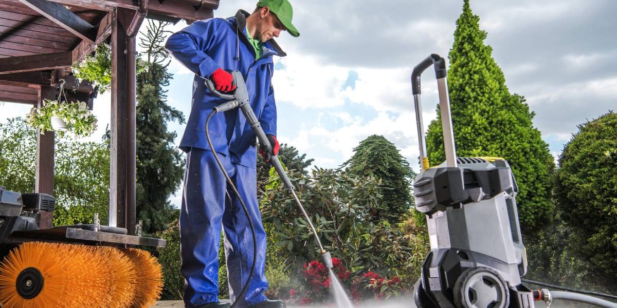 Caucasian Men Washing Residential Bricks Made Driveway and Paths Using Powerful Pressure Washer. Spring Maintenance Theme.