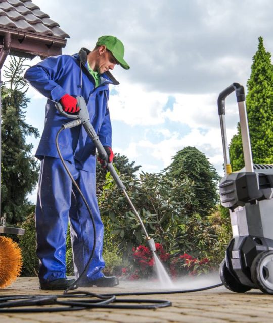 Caucasian Men Washing Residential Bricks Made Driveway and Paths Using Powerful Pressure Washer. Spring Maintenance Theme.