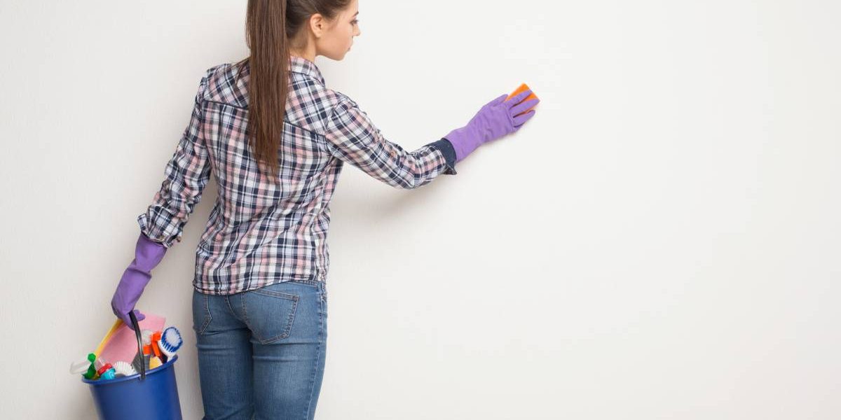 Young woman wiping white wall from dust