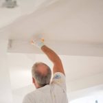 Back view of a handyman painting a wall with a paintbrush