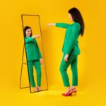 I choose myself. Excited stylish lady pointing finger at her reflection in mirror, yellow background, free space