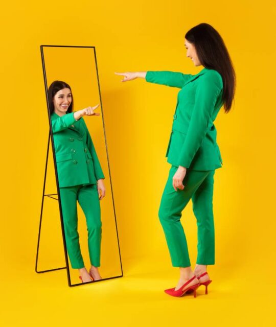 I choose myself. Excited stylish lady pointing finger at her reflection in mirror, yellow background, free space