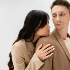Losing a Partner asian woman with long brunette hair hugging man in beige jacket isolated on grey
