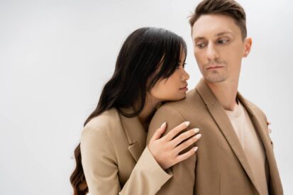 Losing a Partner asian woman with long brunette hair hugging man in beige jacket isolated on grey