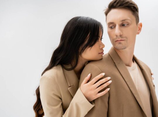 Losing a Partner asian woman with long brunette hair hugging man in beige jacket isolated on grey