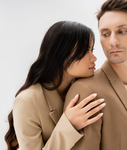 Losing a Partner asian woman with long brunette hair hugging man in beige jacket isolated on grey