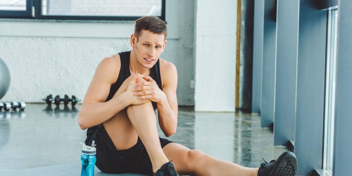 sportsman with injured knee resting on mat in gym