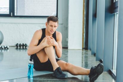 sportsman with injured knee resting on mat in gym