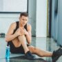sportsman with injured knee resting on mat in gym